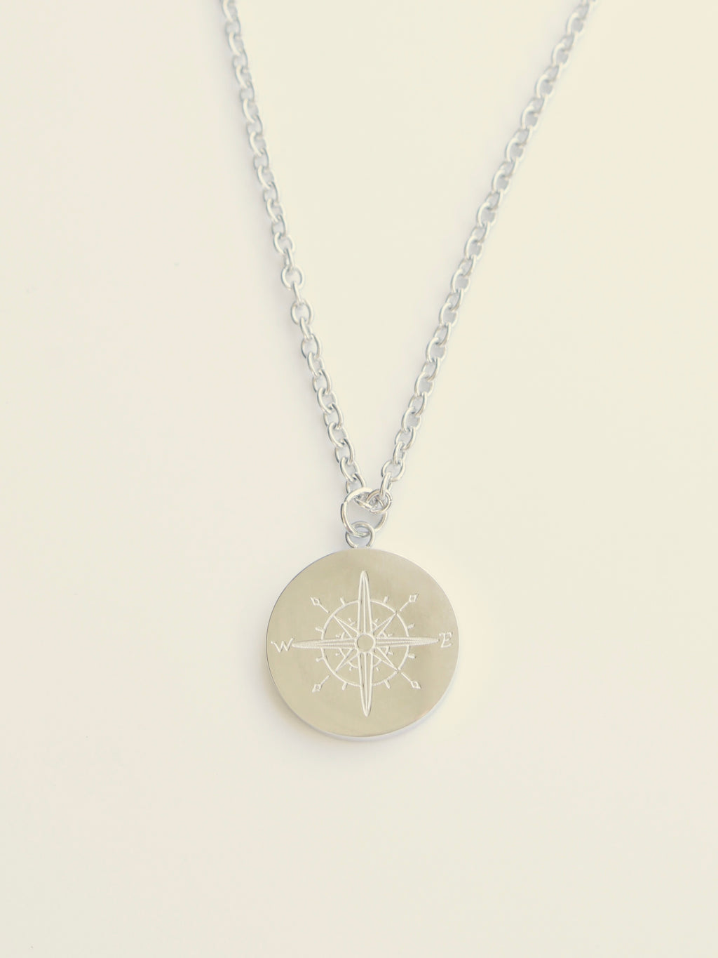 Silver necklace with a round pendant on a beige background
