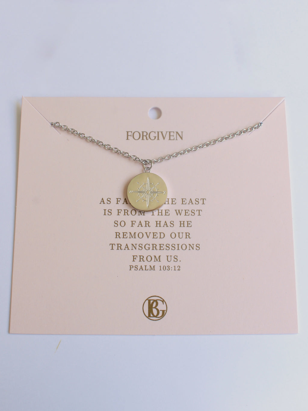 Necklace with a gold pendant on a pink card with text and a logo.