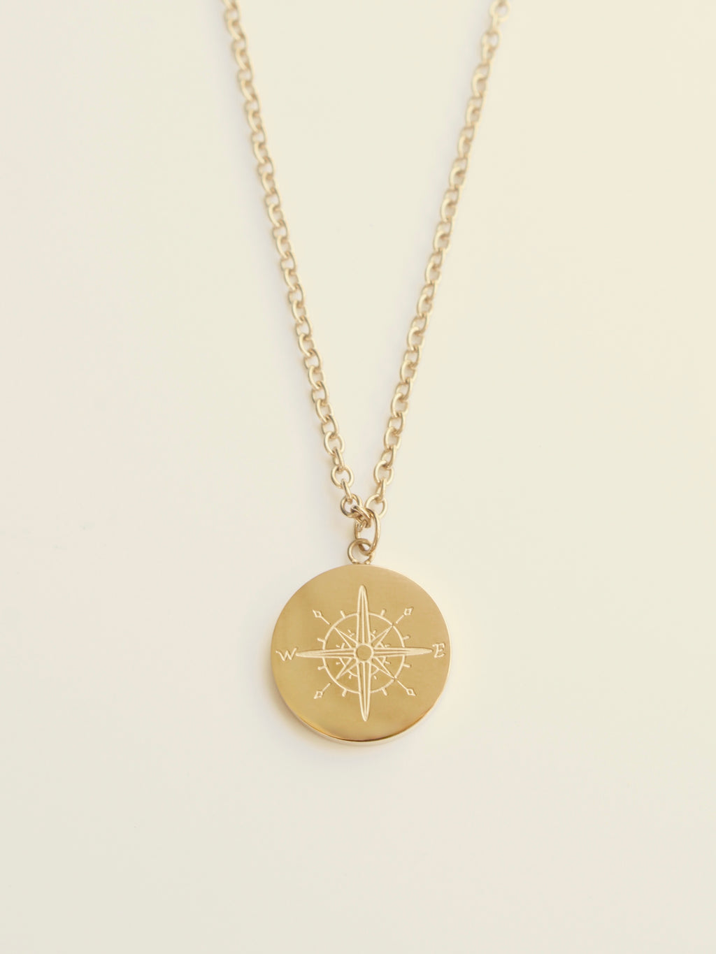 Gold necklace with a compass pendant on a beige background