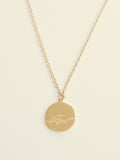 Gold necklace with a round pendant featuring a wave design on a beige background