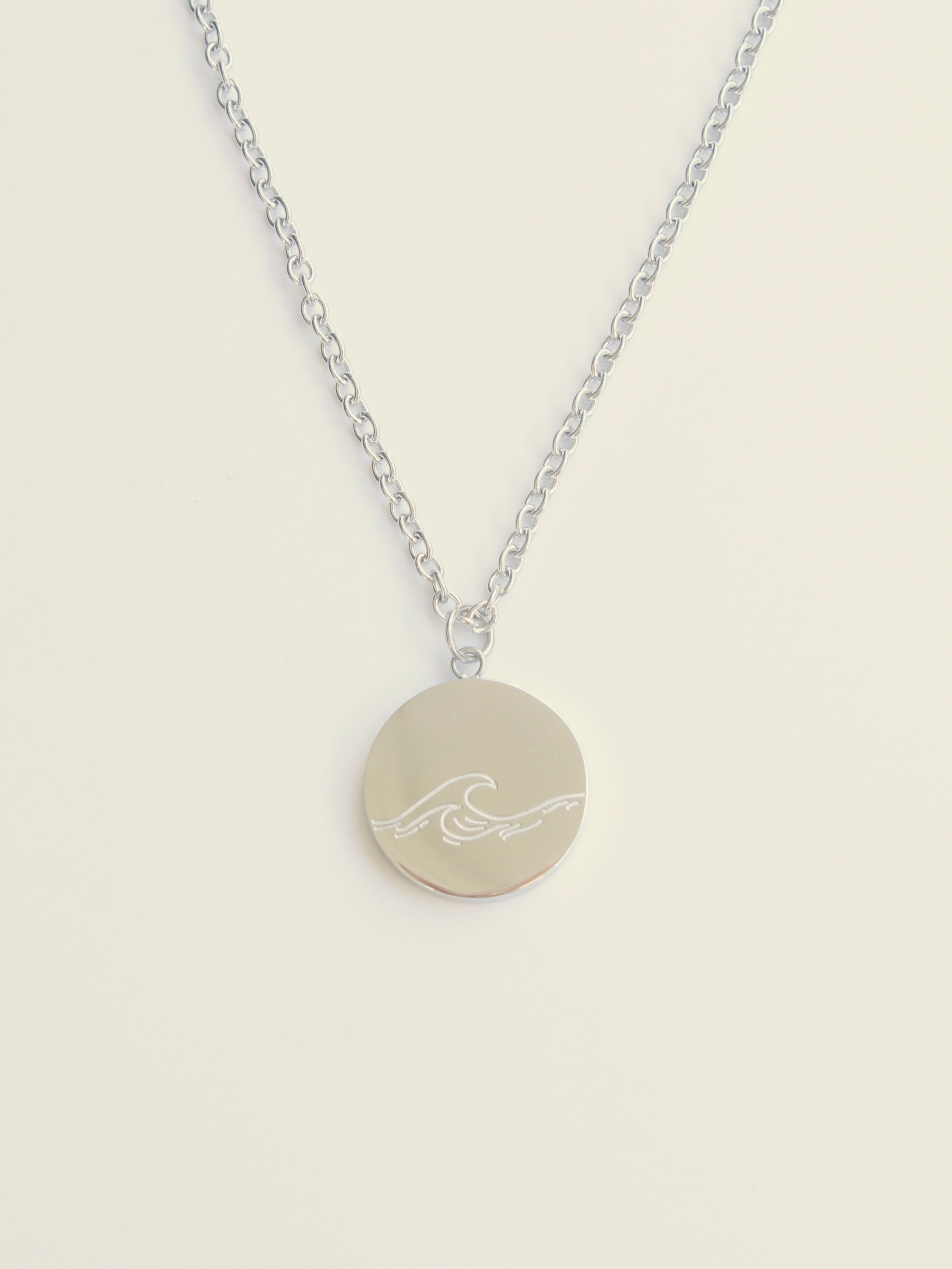 Necklace with a round pendant featuring a wave design on a beige background