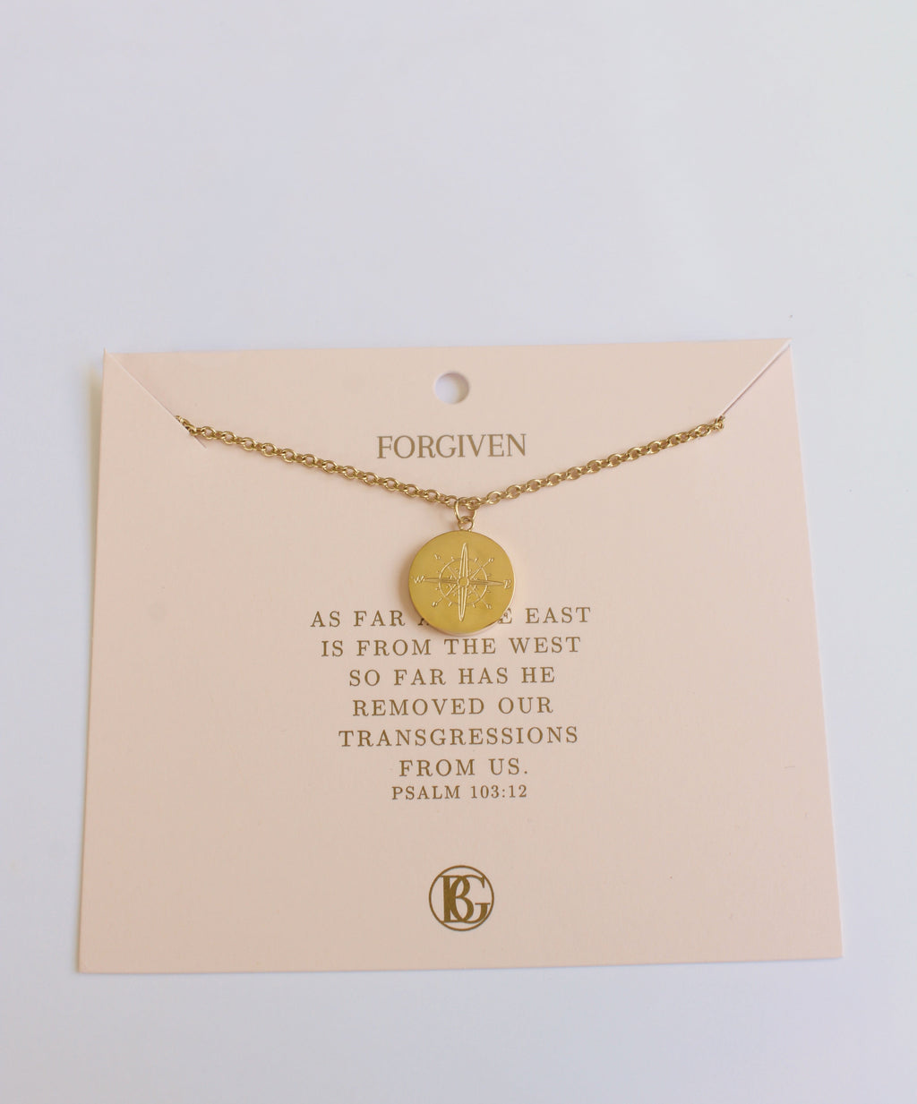 Gold necklace on a card with text and a brand logo, on a light background