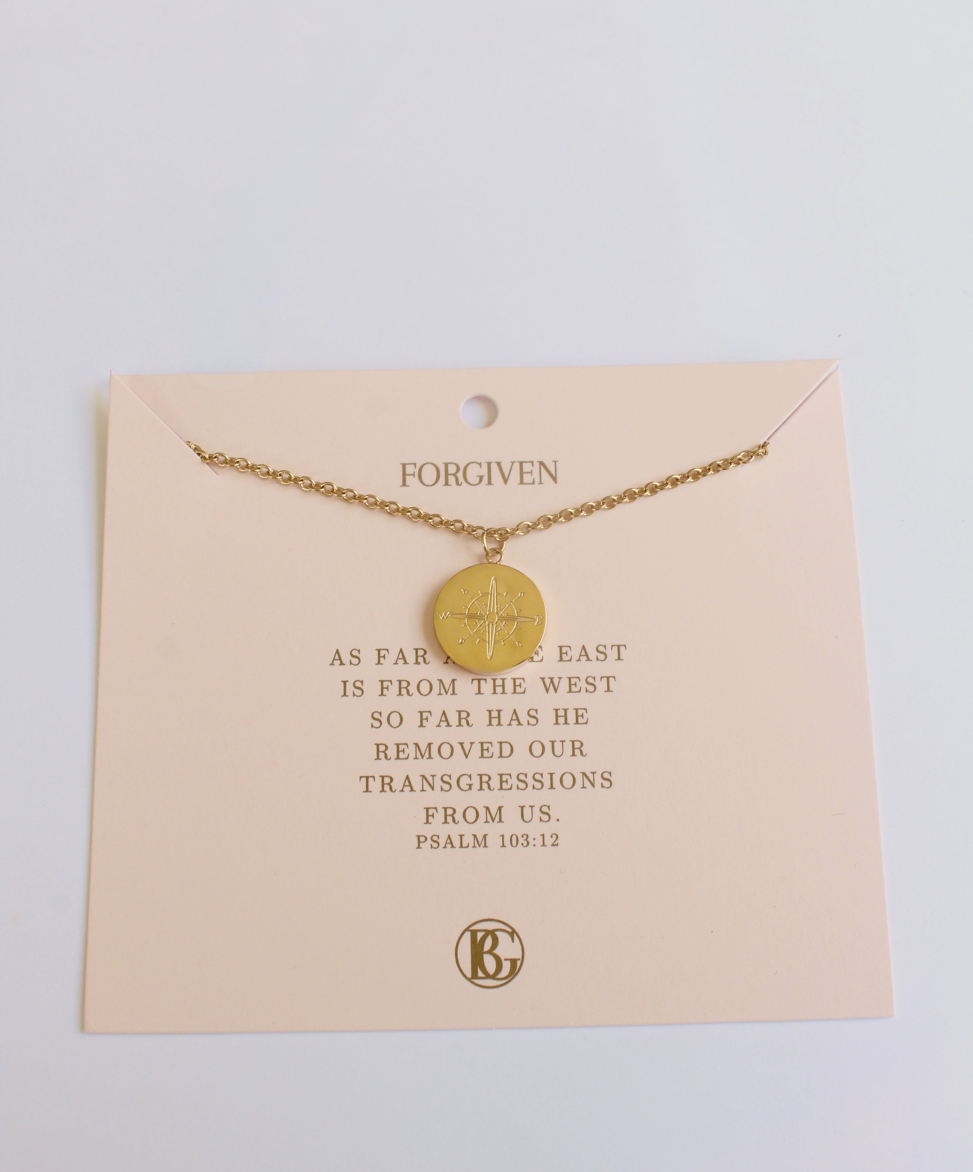 Gold necklace on a card with text and a brand logo, on a light background