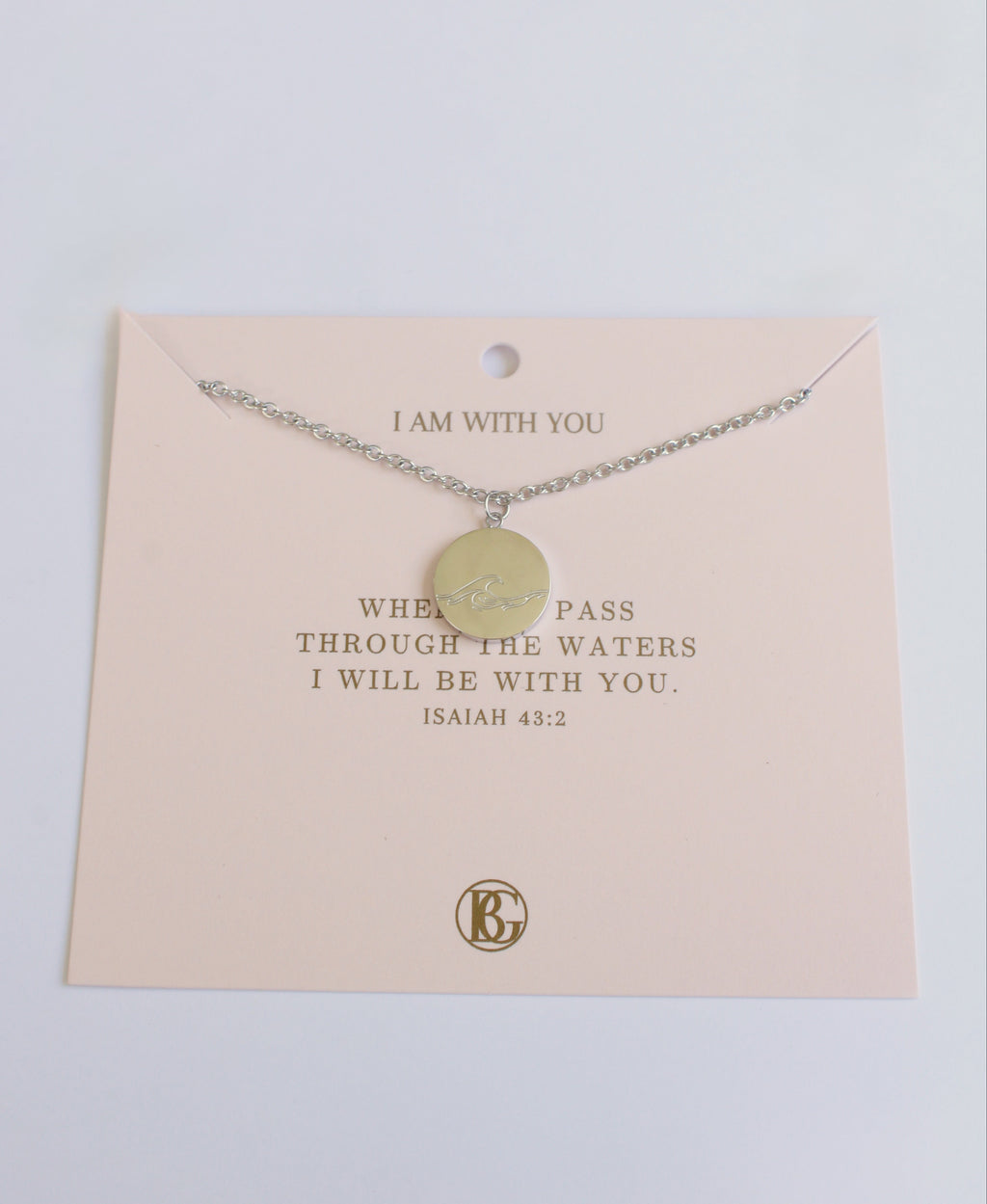 Necklace with a round pendant on a pink card with text, against a light gray background