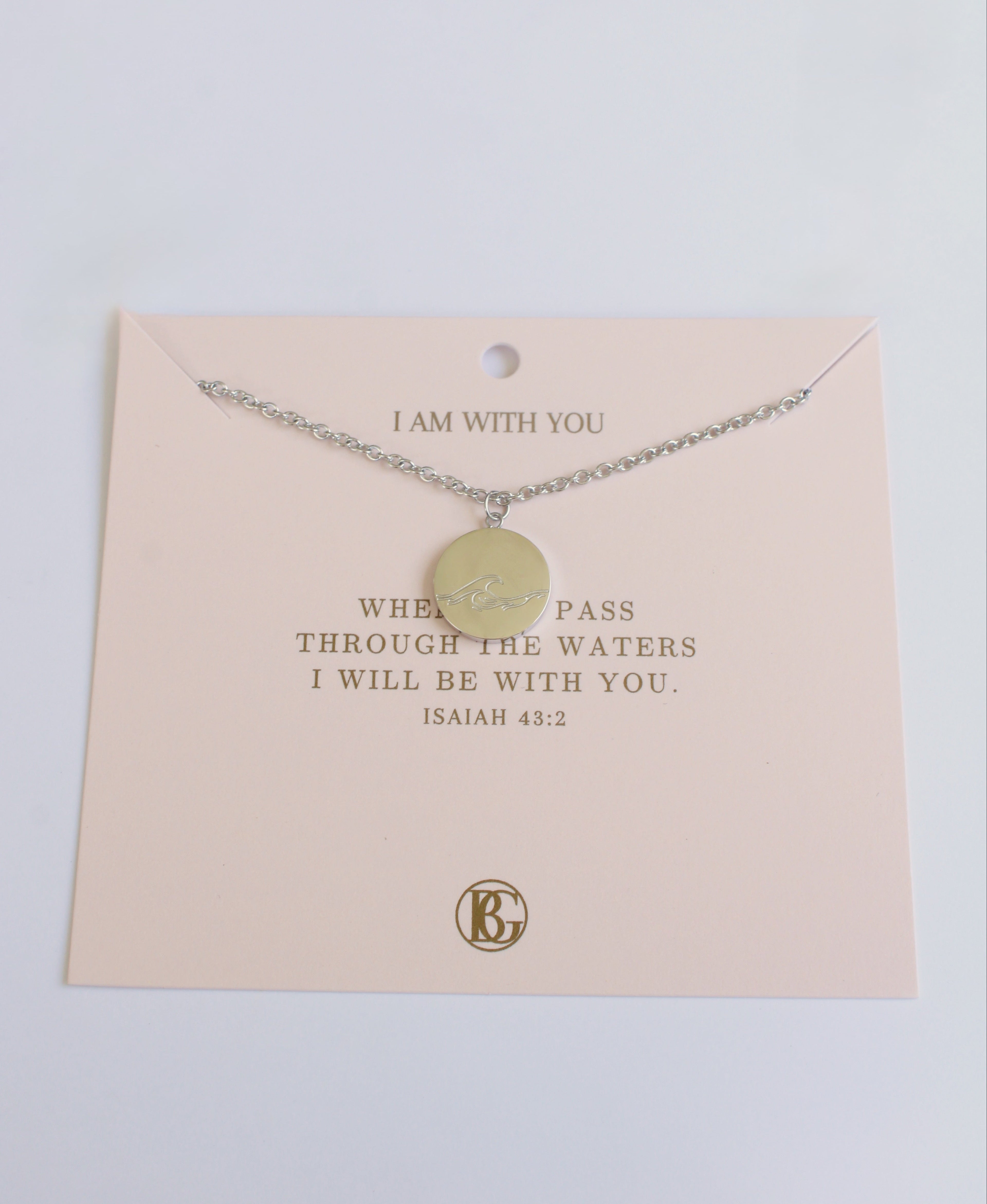 Necklace with a round pendant on a pink card with text, against a light gray background