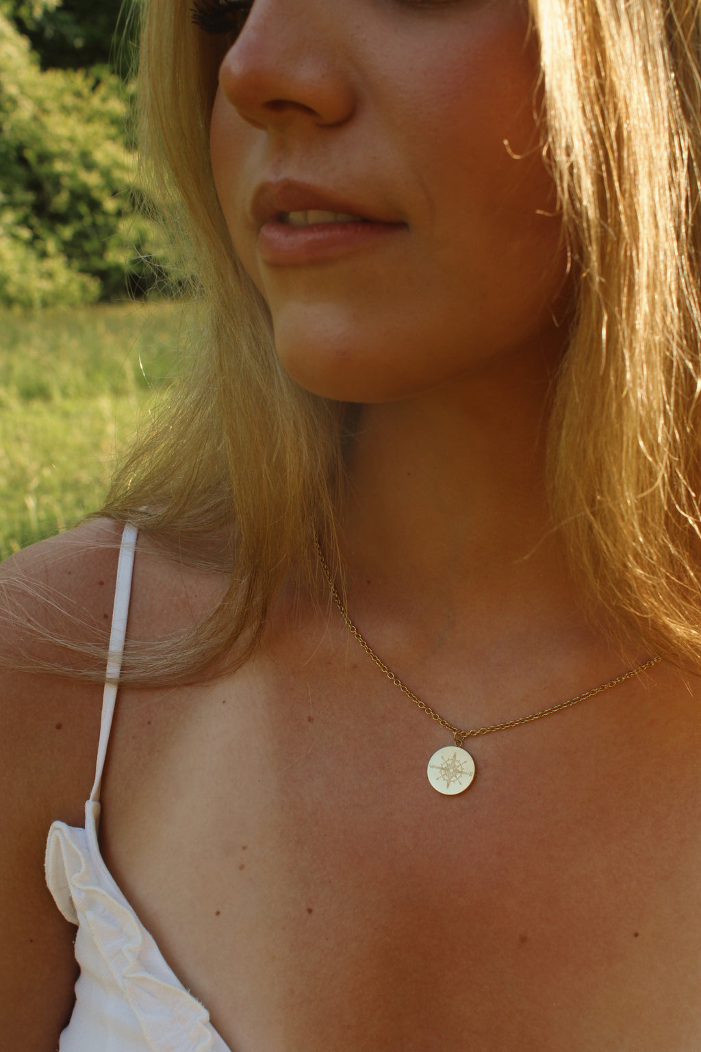 Close-up of a woman wearing a necklace with a circular pendant outdoors.