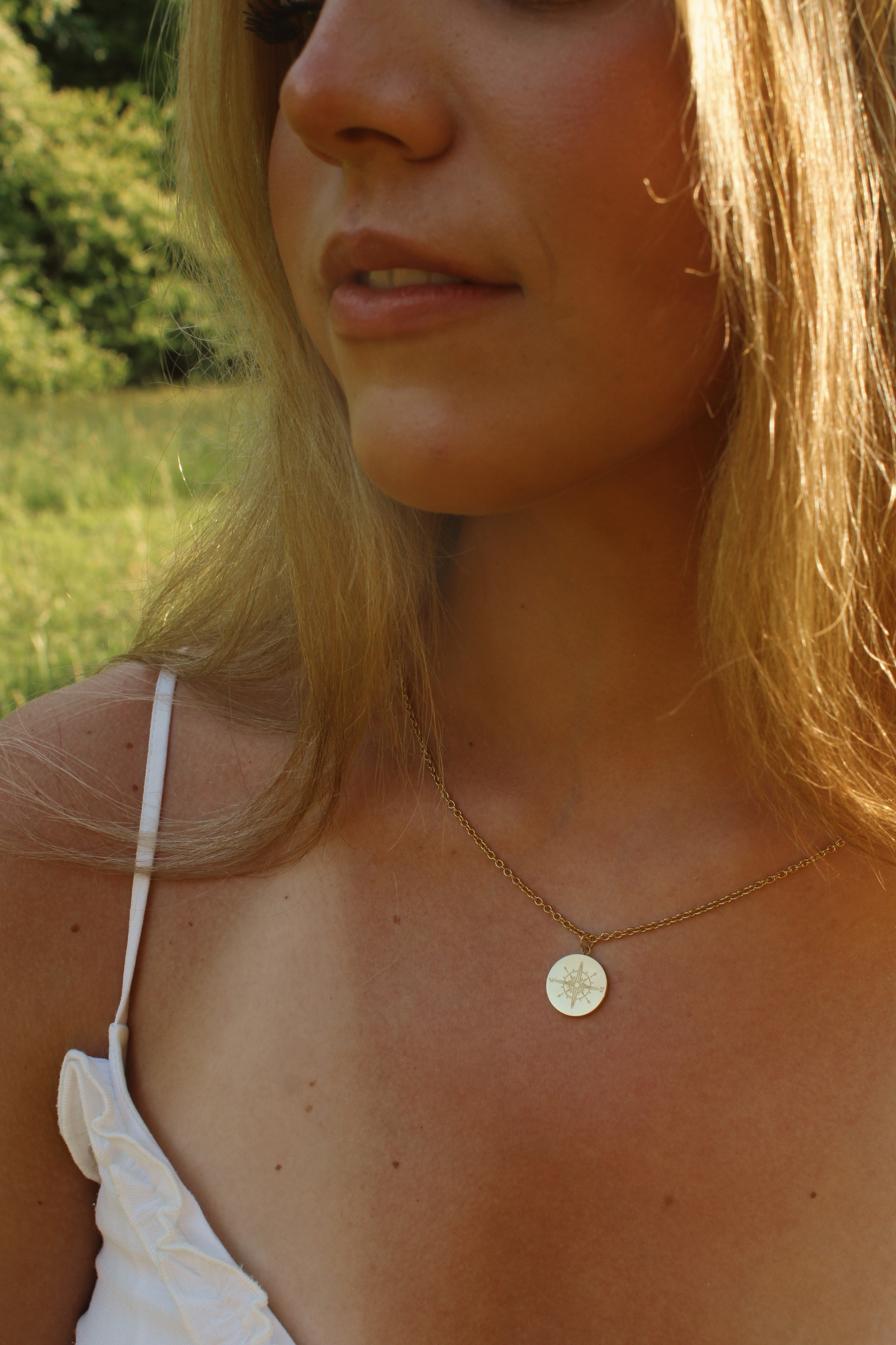 Close-up of a woman wearing a necklace with a circular pendant outdoors.