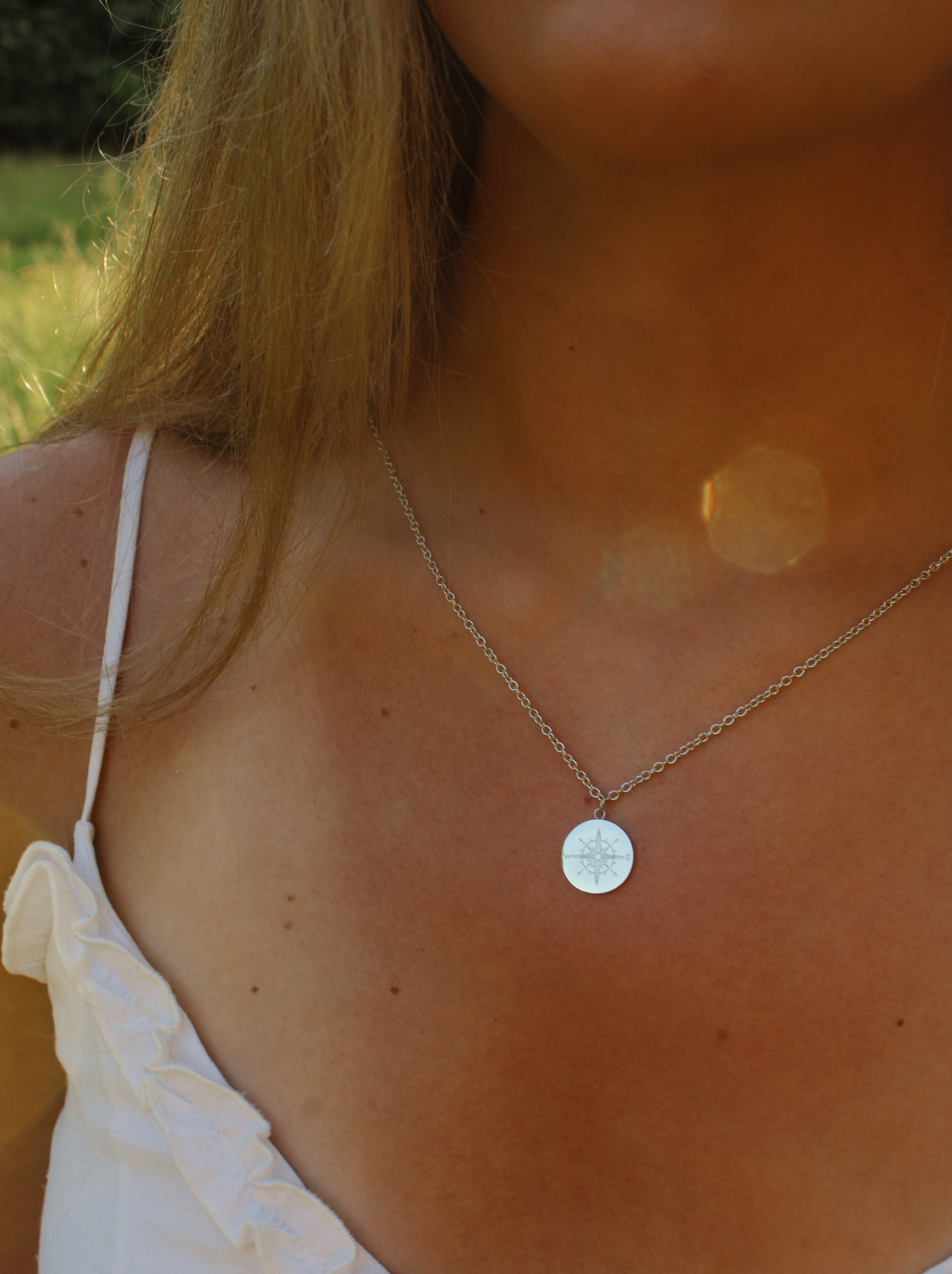 Close-up of a person wearing a silver necklace with a round pendant outdoors.