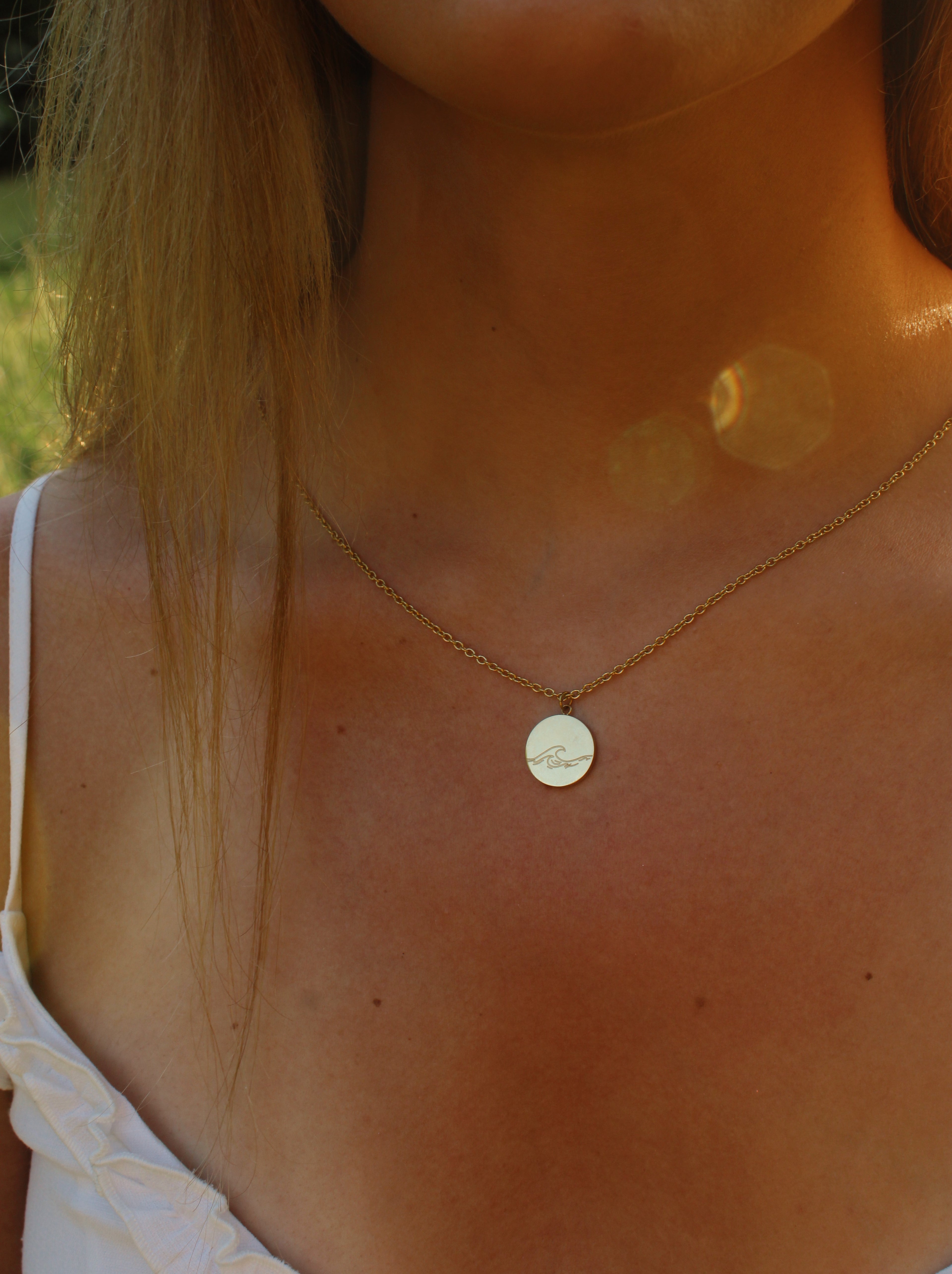 Close-up of a person wearing a gold necklace with a round pendant outdoors.